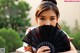 A woman holding a black fan in front of her face.