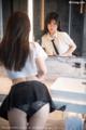 A woman in a white shirt and black skirt looking at herself in the mirror.