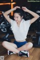 A woman sitting on the floor in a gym with her hands behind her head.