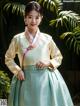 A woman in a green and yellow hanbok poses for a picture.