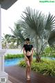 A woman in a black bikini standing next to a pool.