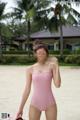 A woman in a pink swimsuit standing on a beach.