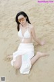 A woman in a white bikini sitting on the sand.