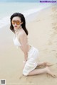 A woman in a white bikini sitting on the beach.