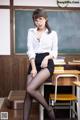 A woman in a white shirt and black skirt sitting at a desk.