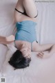 A woman laying on a bed in a blue top and black panties.