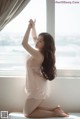 A woman sitting on a bed in front of a window.