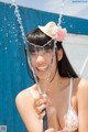 A woman in a bikini and a straw hat is holding a hose.