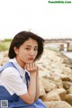 A woman in a blue dress sitting on a rock by the water.