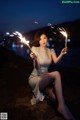 A woman sitting on a rock holding a sparkler.