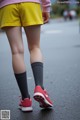 A person wearing yellow shorts and a pink sweater is walking down the street.