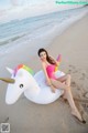 A woman in a pink bikini sitting on an inflatable unicorn on the beach.