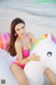 A woman in a pink bikini sitting on an inflatable unicorn.