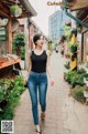 A woman walking down a street in a black tank top and jeans.