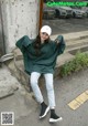 a woman sitting on the steps of a building wearing a green sweatshirt and jeans