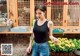 A woman standing in front of a flower shop holding a purse.