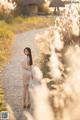 A woman in a beige dress standing on a dirt road.