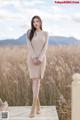 A woman in a beige sweater dress standing on a wooden platform.