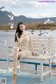 A woman sitting on a bench with seagulls flying around her.