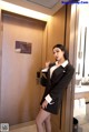 A woman in a black suit standing in front of a door.