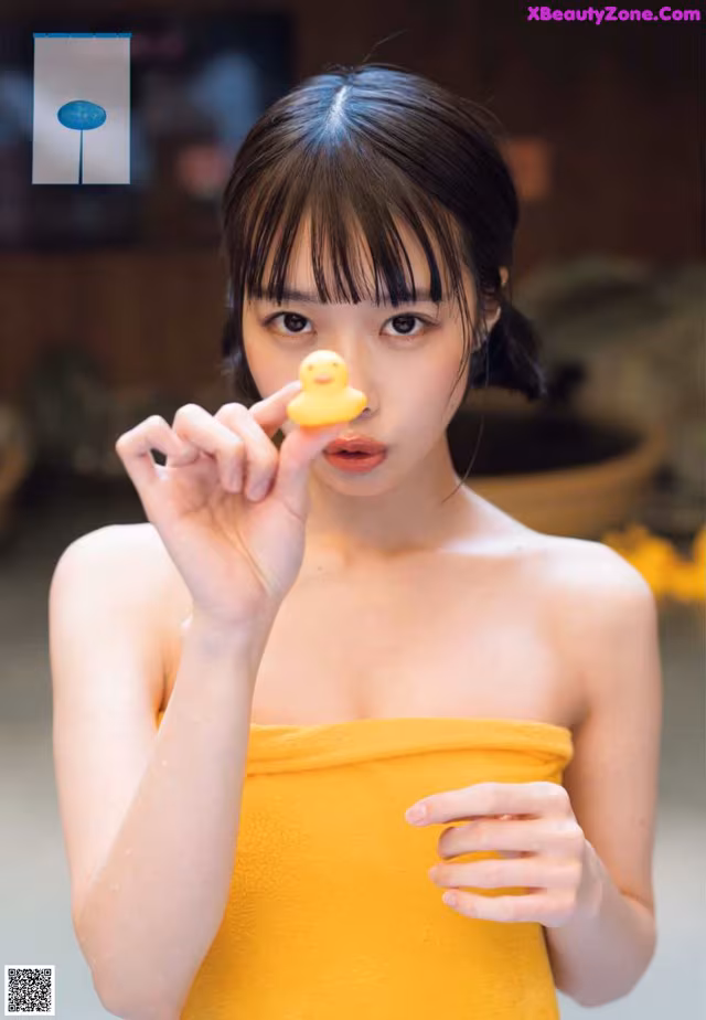 A woman in a yellow towel holding a yellow rubber duck.