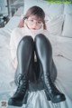 A woman sitting on a bed wearing black leather pants and boots.